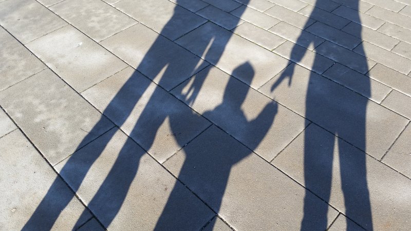 Shadows of a family holding hands on a paved walkway